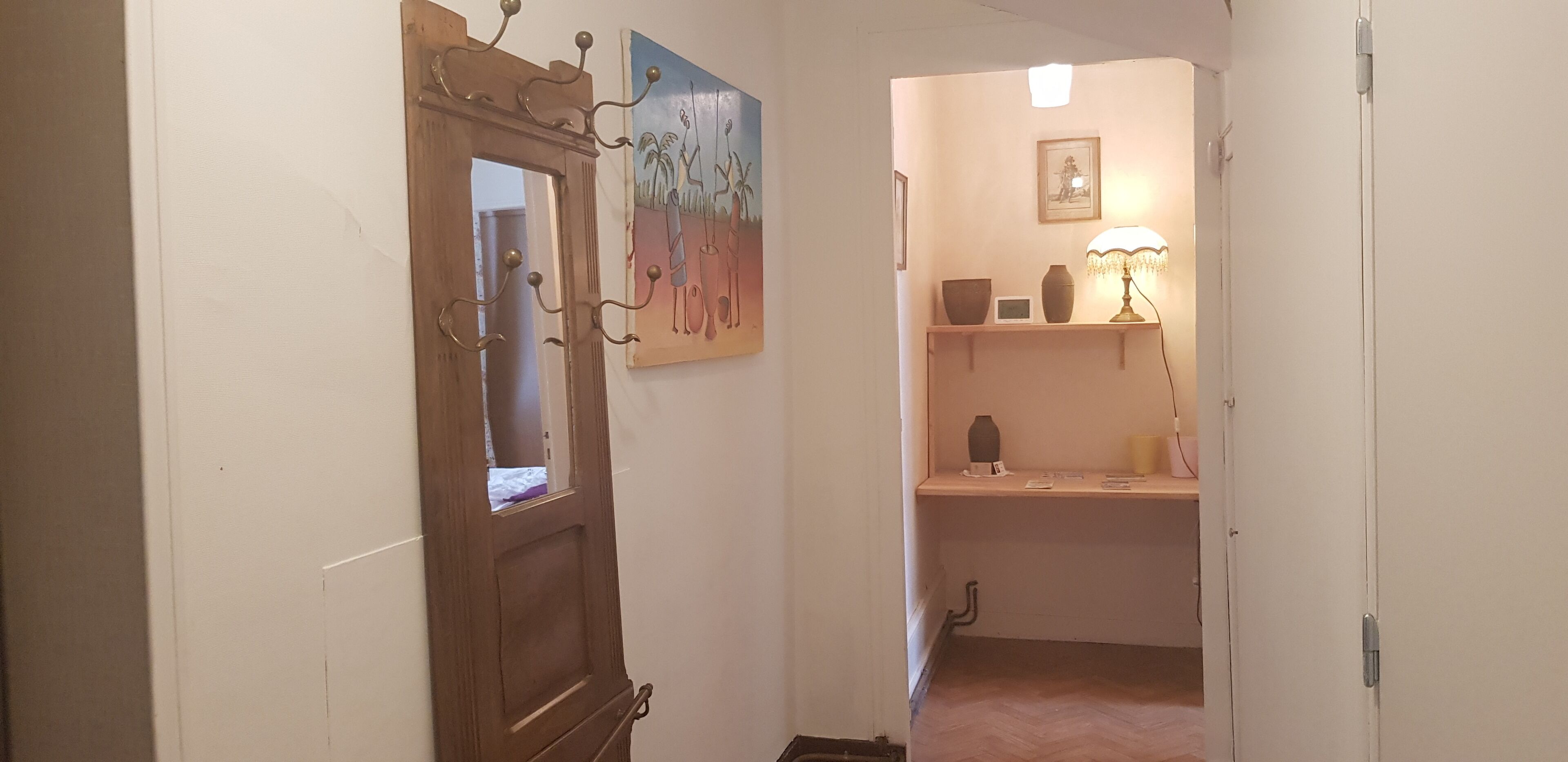A hallway with a wooden door, a painting, a shelf with decorative items, and a lamp.