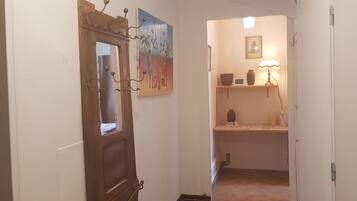 A hallway with a wooden door, a painting, a shelf with decorative items, and a lamp.