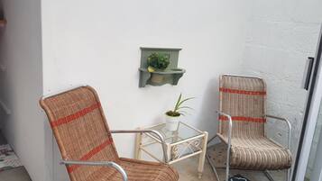 A small balcony with two wicker chairs, a glass table, and a potted plant.