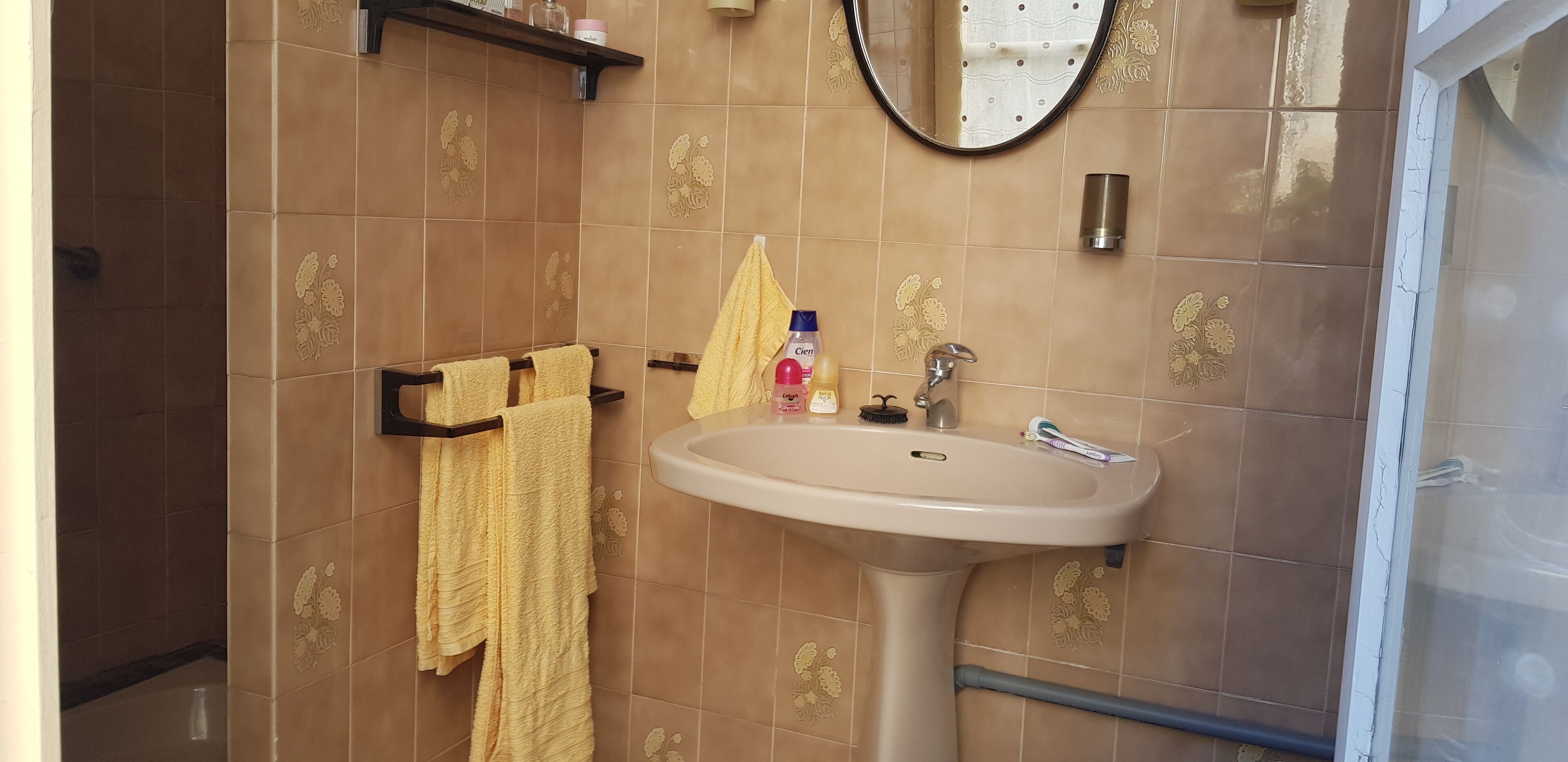 Et badeværelse med beige fliser, en vask, et spejl og en håndklædestang.