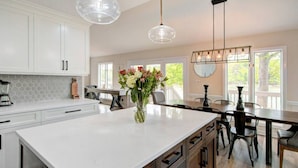Una cocina moderna con armarios blancos, una isla grande y un comedor con mesa y sillas de madera.
