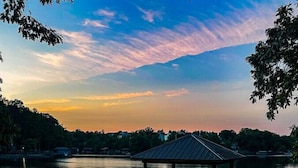 Un jacuzzi con terraza de madera y un pabellón, con vistas a un lago tranquilo al atardecer.