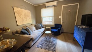 A living room with a sofa, a blue armchair, a coffee table, a world map on the wall, and a television on a dresser. - Cozy Court Street #2 (Fayetteville)