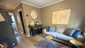 A living room with a sofa, two round tables, a coffee machine, and a world map on the wall. - Cozy Court Street #2 (Fayetteville)