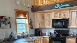 A kitchen with wooden cabinets, a large island with bar stools, a microwave, and a toaster.