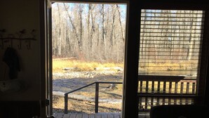 An open door leading to a deck with a view of a forest and a river.