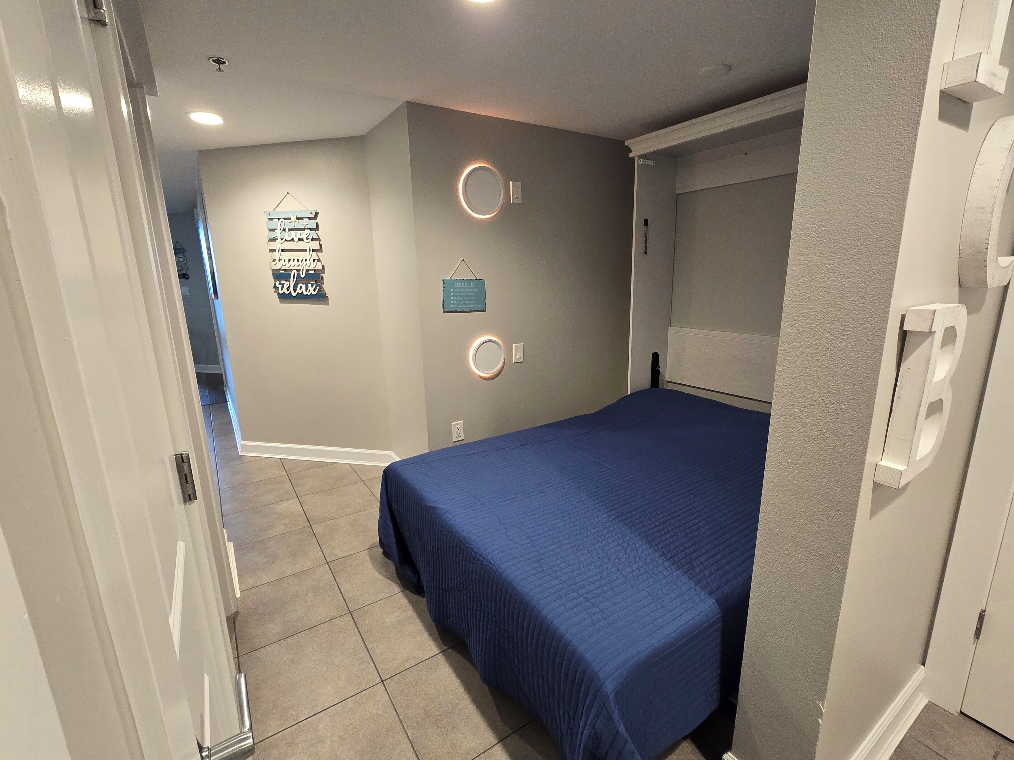 Une chambre à coucher avec un lit, une porte, un mur orné d’une enseigne et un luminaire.