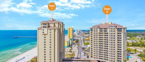 Dos edificios altos con balcones, una playa y un muelle al fondo.