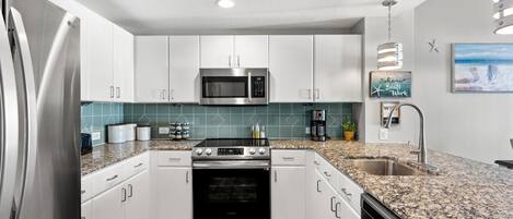 Una cocina moderna con armarios blancos, un refrigerador de acero inoxidable, un microondas, un horno y una encimera de granito.