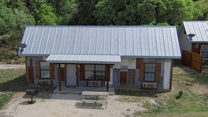 A rustic cabin with a metal roof, large windows, and a front porch. - Hunter's Ridge Cabins - 2 (Concan)