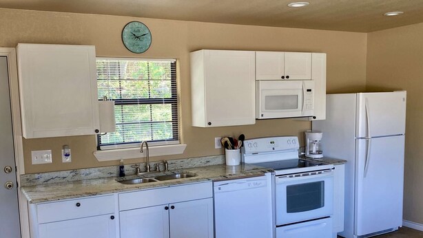 A compact kitchen with white cabinets, a microwave, a refrigerator, and a clock on the wall. - Hunter's Ridge Cabins - 2 (Concan)