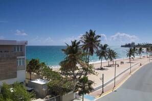 A beach view with palm trees, a clear sky, and a building adjacent to the beach.