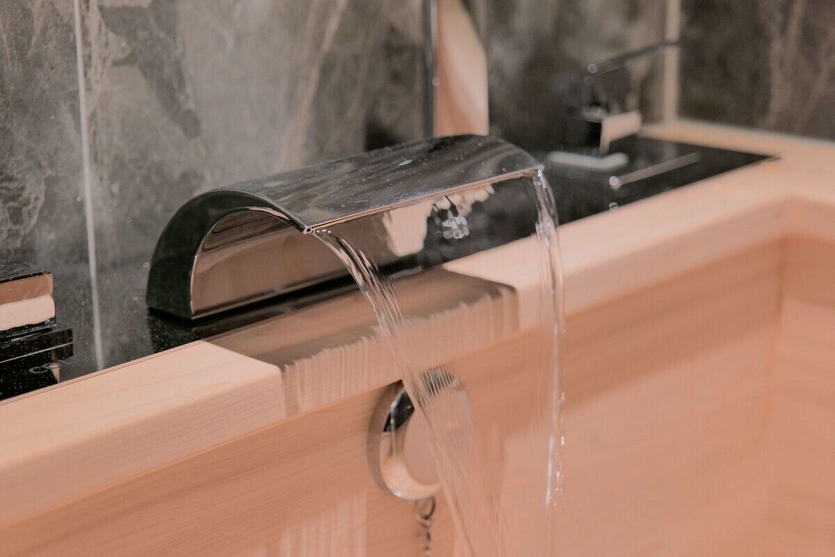 A modern bathroom with a marble backsplash, a wooden vanity, and a black faucet.