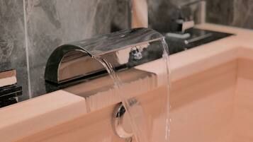 A modern bathroom with a marble backsplash, a wooden vanity, and a black faucet.