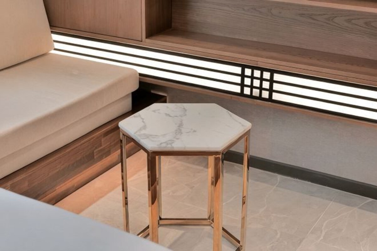 A marble-topped table with gold legs, a beige sofa, and wooden paneling with a light strip.