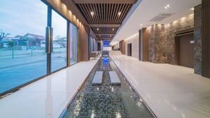 Ein moderner Hotelkorridor mit Glaswand, einem gefliesten Wasserspiel und einer Decke mit linear angeordneten Leuchten.