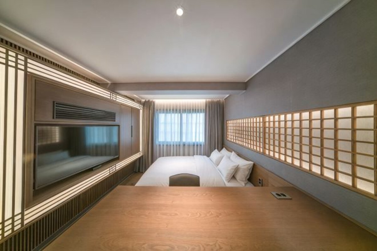 A modern hotel room with a large bed, a TV, and a wooden floor.