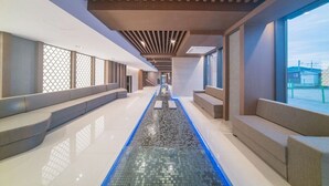 Ein moderner Wellnessbereich mit einem langen, schmalen Pool, gepolsterten Sitzgelegenheiten und großen Fenstern.