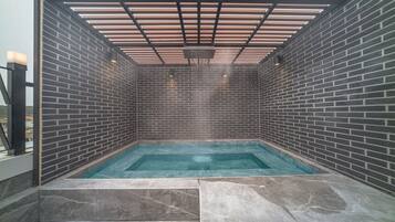 Une piscine intérieure moderne, entourée d’un mur en briques, dotée d’un toit en forme de pergola et offrant une vue dégagée sur les environs.