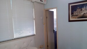 A bedroom with a bed, a window with blinds, a door, and a framed picture on the wall. - Kris Hotel (PETROLINA)