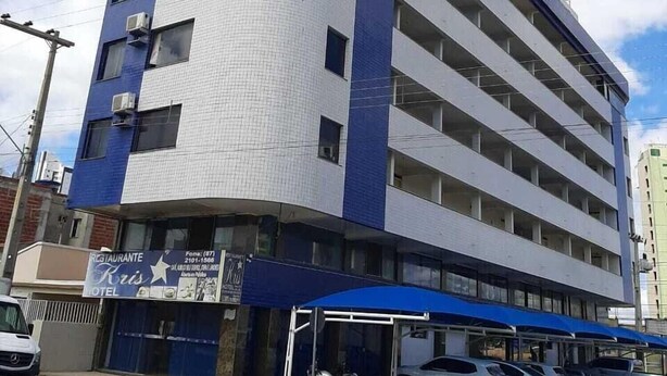 A multi-story hotel with a curved facade, several balconies, and a covered parking area with cars. - Kris Hotel (PETROLINA)
