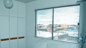 A bedroom with a bed, a window with blinds, and a view of buildings outside. - Kris Hotel (PETROLINA)