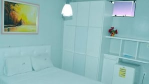 A bedroom with a bed, a bedside table, a small cabinet, a wall-mounted TV, and a painting. - Kris Hotel (PETROLINA)