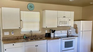 A compact kitchen with white cabinets, a microwave, a refrigerator, a stove, and a sink. - Hunter's Ridge Cabins - 3 (Concan)