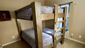 A bunk bed with patterned bedding in a room with beige walls and a tiled floor. - Hunter's Ridge Cabins - 3 (Concan)