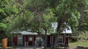 A rustic cabin with a gravel driveway, a wooden fence, and a large tree in front. - Hunter's Ridge Cabins - 3 (Concan)