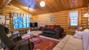 Interior de una cabaña de troncos con una sala de estar acogedora, paredes de madera, chimenea y un ventanal con vistas.