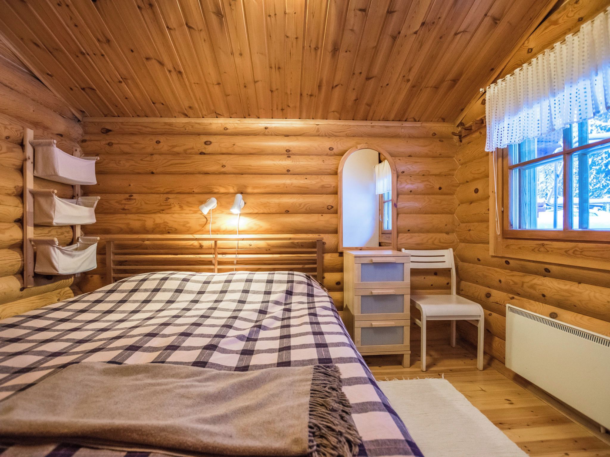 Un dormitorio rústico de cabaña con una cama, lámparas de noche, un tocador y una ventana con cortinas.