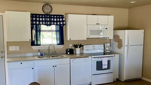A compact kitchen with white cabinets, a microwave, a refrigerator, a stove, and a sink.