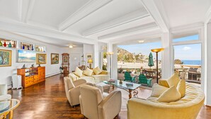 Amplia sala de estar con un ventanal que ofrece una vista panorámica, una zona de estar acogedora con sofá y sillones, y un mueble de madera con objetos decorativos.