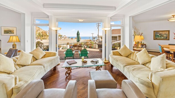 Amplia sala de estar con un gran ventanal que da a un patio exterior. Hay dos sofás beige, una mesa de centro de cristal y una mesa de comedor con sillas.