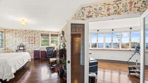 Una habitación con cama, escritorio, silla, ventana con vistas y un telescopio.