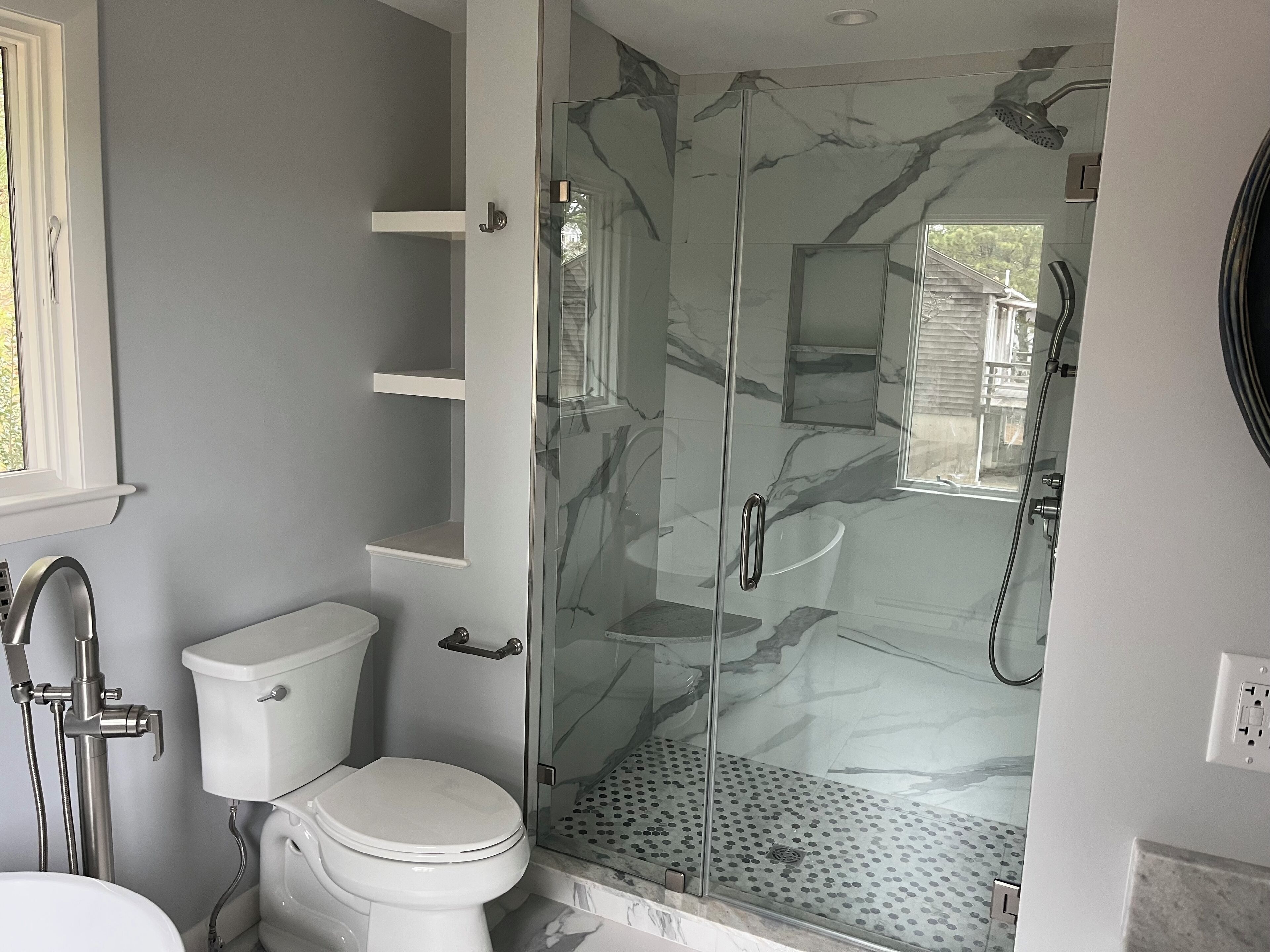 A bathroom with a toilet, a glass-enclosed shower, and a marble backsplash.