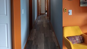 A hallway with wooden flooring, a yellow chair, and a door on the left.