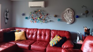 A red leather sofa with colorful pillows, a wall clock, and a decorative wall piece. - Centrally located to everything Fish Creek has to offer (Fish Creek)