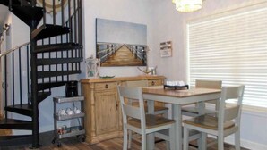 Un coin repas avec une table et des chaises en bois, un escalier, un lustre et un tableau au mur.