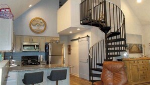 Une cuisine moderne dotée d’un îlot central, d’un escalier en colimaçon et d’un coin repas avec des tabourets de bar.