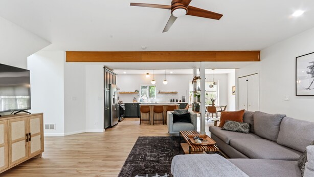 Ein modernes Wohnzimmer mit einer Couch, einem Couchtisch und einem Fernseher. Im Hintergrund befindet sich eine Küche mit einem Essbereich.