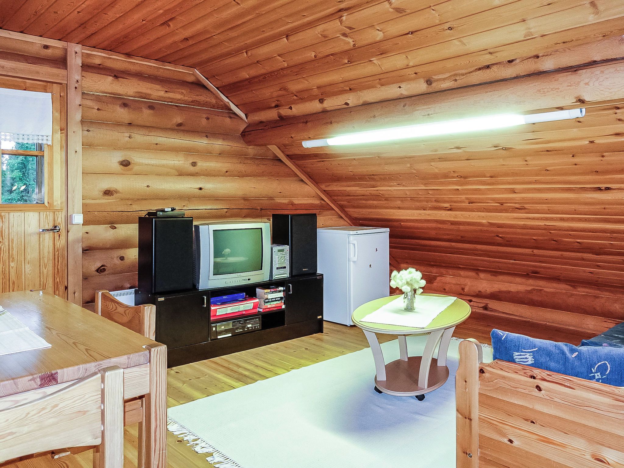A wooden interior with a television, books, and a small table with a vase.