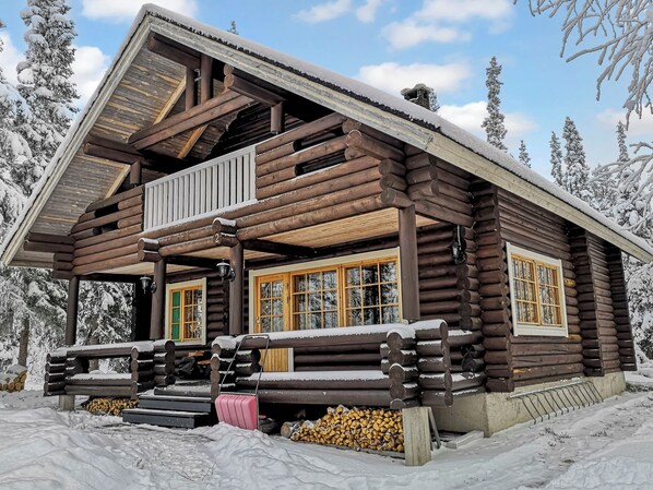 A log cabin with a balcony, large windows, and a snow-covered landscape.