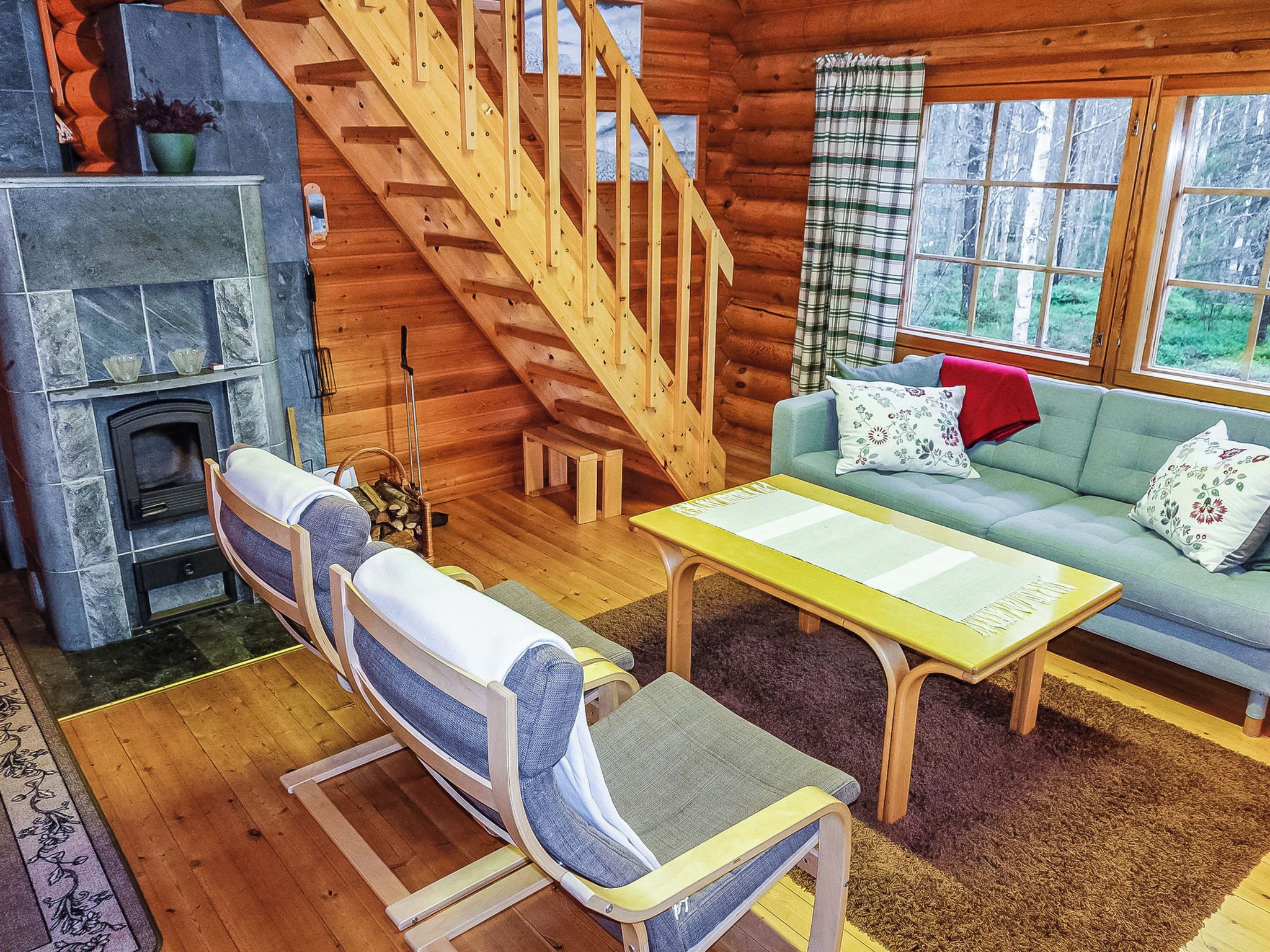 A log cabin interior with a stone fireplace, a wooden staircase, a sofa with cushions, and a coffee table.