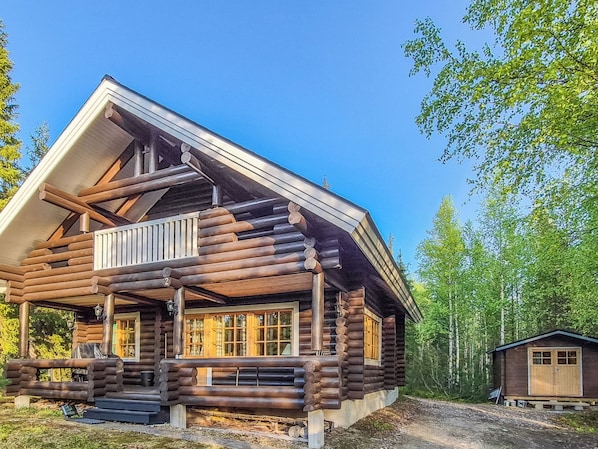 A log cabin with a porch, a chimney, and a small adjacent shed.