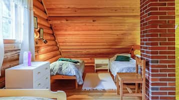 A cozy attic bedroom with wooden walls, a brick fireplace, two beds, a desk, and a chair.