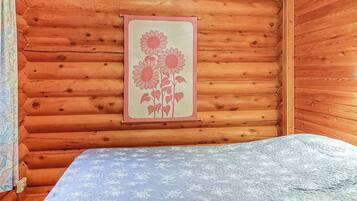 Interior de cabana de madeira, com uma cama, quadro de flores na parede e colcha estampada.