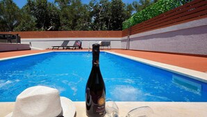 A pool area with a bottle of wine, a glass, and a hat on a table.