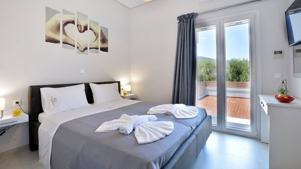 A modern hotel room with a large bed, a flat-screen TV, a balcony with a view, and a ceiling light fixture.